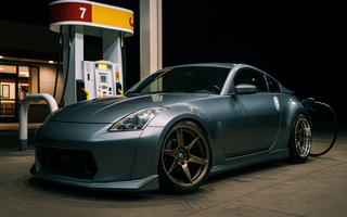 Slammed Nissan 350Z with a wide body kit parked at a gas station at night, front wheels turned 90 degrees showing extreme steering angle