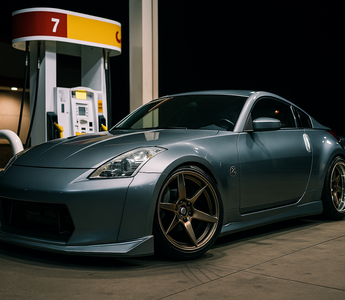 Slammed Nissan 350Z with a wide body kit parked at a gas station at night, front wheels turned 90 degrees showing extreme steering angle