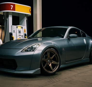 Slammed Nissan 350Z with a wide body kit parked at a gas station at night, front wheels turned 90 degrees showing extreme steering angle