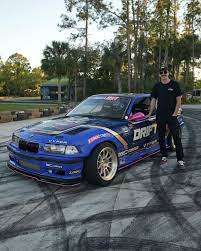 Adam LZ's BMW E36 drift car with SLR angle kit during a tandem drift event, Adam LZ standing next to his car.