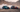 BMW E36 and BMW E46 drift cars with full racing livery sliding in tandem through the Oman desert, throwing tire smoke during a high speed drift run, wide 16:9 motorsport action scene