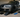 A lowered sports car positioned on split-style race ramps in a garage, with an oil drain pan and tools beside it