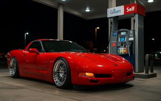 Slammed red C5 Corvette parked at a gas station pump at night, reflecting neon lights on the wet pavement with an aggressive stance and lowered coilover suspension.