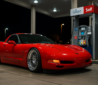 Slammed red C5 Corvette parked at a gas station pump at night, reflecting neon lights on the wet pavement with an aggressive stance and lowered coilover suspension.