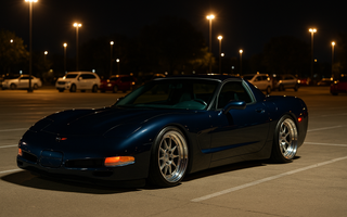 Slammed navy blue C5 Corvette on polished multi-piece wheels parked at a nighttime car meet under bright parking lot lights on SLR coilovers