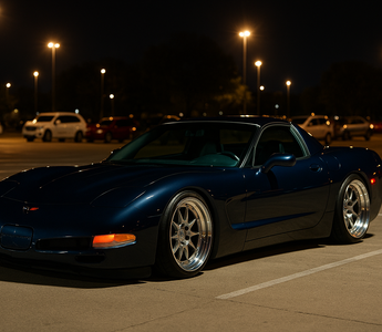 Slammed navy blue C5 Corvette on polished multi-piece wheels parked at a nighttime car meet under bright parking lot lights on SLR coilovers