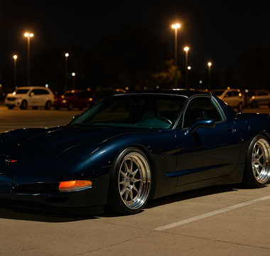 Slammed navy blue C5 Corvette on polished multi-piece wheels parked at a nighttime car meet under bright parking lot lights on SLR coilovers