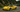 Slammed yellow C5 Corvette with wide body kit and large rear wing rolling through a winding mountain road, captured in a dynamic cornering shot.