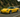 Slammed yellow C5 Corvette with wide body kit and large rear wing rolling through a winding mountain road, captured in a dynamic cornering shot.