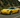 Slammed yellow C5 Corvette with wide body kit and large rear wing rolling through a winding mountain road, captured in a dynamic cornering shot.