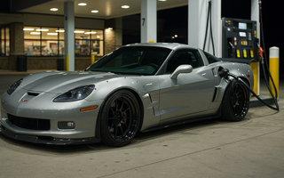 Slammed widebody C6 Corvette Z06 parked at a gas station pump at night, featuring lowered stance, aggressive aero, deep-dish wheels, and performance-focused styling.