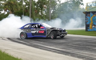 Drift car mid-slide with front wheels countersteered and smoke pouring off rear tires at full opposite lock