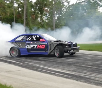 Drift car mid-slide with front wheels countersteered and smoke pouring off rear tires at full opposite lock