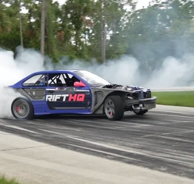 Drift car mid-slide with front wheels countersteered and smoke pouring off rear tires at full opposite lock