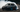 A professional drift car sliding sideways at full lock with smoke pouring from the rear tires during a drift event