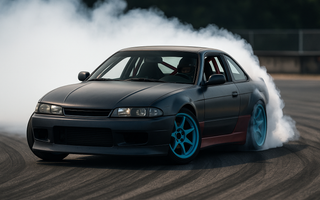 A professional drift car sliding sideways at full lock with smoke pouring from the rear tires during a drift event