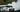 A drift car mid-corner with smoke pouring from the rear tires on a wide race track, captured during a clutch kick initiation