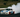 A drift car mid-corner with smoke pouring from the rear tires on a wide race track, captured during a clutch kick initiation