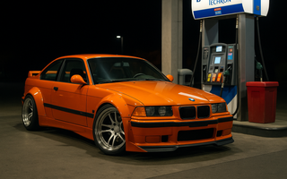 Orange widebody BMW E36 M3 slammed at a gas station pump at night with the front wheels turned, showcasing aggressive stance, drift fitment, and performance styling with E36 angle kit.