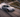 BMW E46 drift car sliding on mountain pass with high steering angle and tire smoke viewed from drone