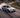 BMW E46 drift car sliding on mountain pass with high steering angle and tire smoke viewed from drone
