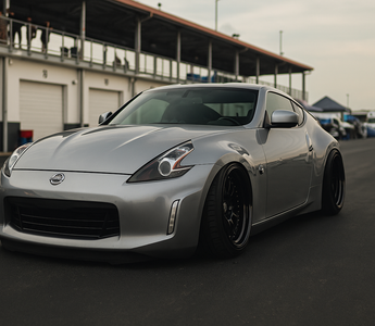 Slammed Nissan 370Z with adjustable coilovers displayed at a motorsport paddock showing camber plates, ride height, and performance stance.