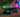 Slammed BMW E46 with a wide body kit and huge rear wing rolling through a Miami Beach street, captured mid corner with palm trees and neon lighting in the background.
