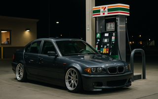 Slammed BMW E46 sedan on large wheels parked under bright 7-Eleven gas station lights at night.