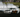 A drift car mid-slide with smoke, countersteer, and crowd in background at a drift track
