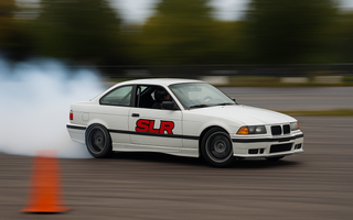 Rear-wheel-drive car initiating a controlled drift around a cone during a drift clinic