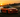 Drift car sliding through a corner in controlled oversteer, smoke rolling off rear tires on a racetrack during sunset
