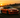 Drift car sliding through a corner in controlled oversteer, smoke rolling off rear tires on a racetrack during sunset