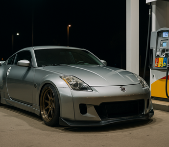Slammed silver Nissan 350Z with a wide body kit parked at a gas station pump at night, illuminated by neon lights reflecting off wet pavement, showcasing aggressive stance and lowered coilover suspension.