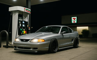 Slammed SN95 drift car parked at a 7-Eleven gas station pump at night under bright canopy lights.