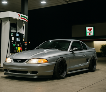 Slammed SN95 drift car parked at a 7-Eleven gas station pump at night under bright canopy lights.