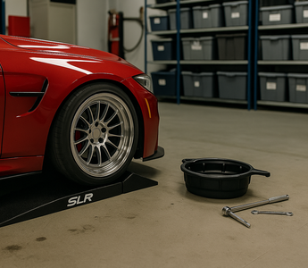 A low-profile sports car on SLR split race ramps in a garage, with jack and tools nearby